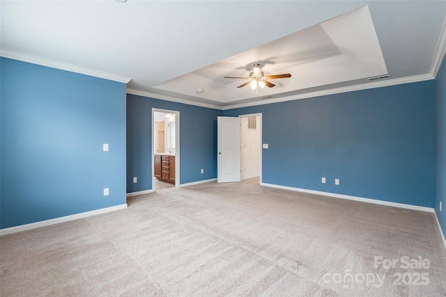 unfurnished bedroom with ornamental molding, light colored carpet, ceiling fan, a tray ceiling, and ensuite bath