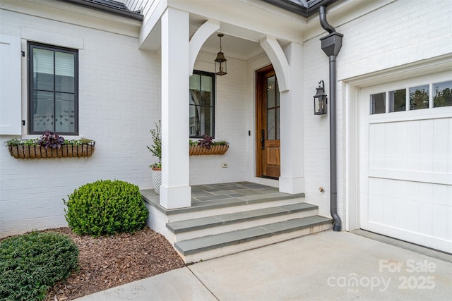 doorway to property featuring a porch, brick siding, and a garage