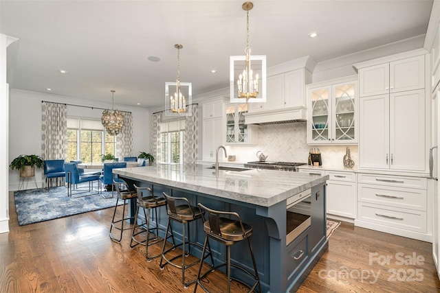 kitchen with dark wood finished floors, light stone counters, ornamental molding, white cabinetry, and a sink