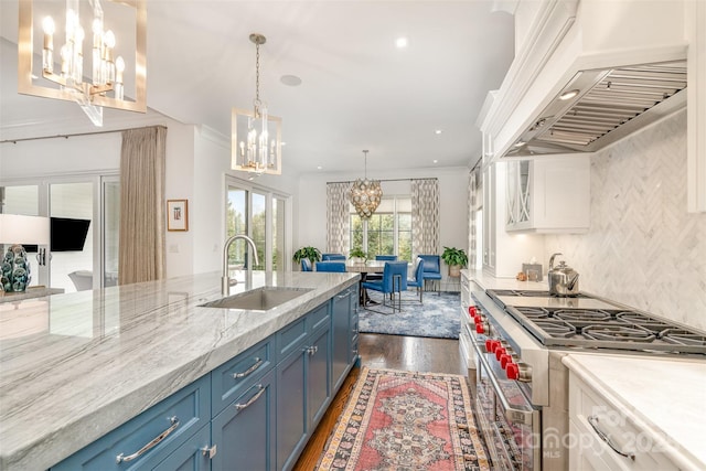 kitchen featuring stainless steel range, an inviting chandelier, blue cabinetry, premium range hood, and a sink