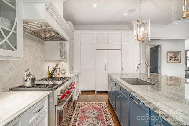 kitchen with premium appliances, blue cabinets, premium range hood, a sink, and white cabinetry