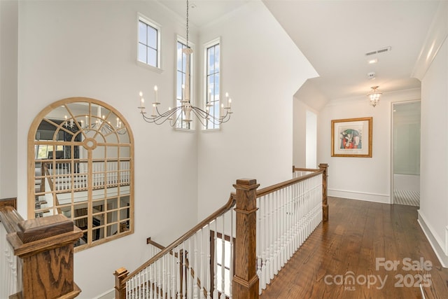 hall with visible vents, baseboards, wood finished floors, crown molding, and an upstairs landing