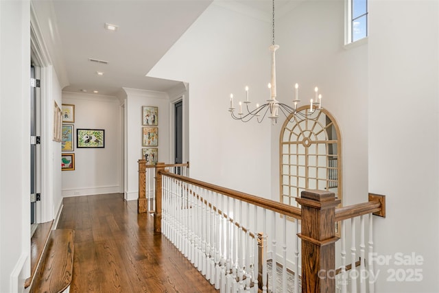 corridor featuring dark wood-style flooring, visible vents, baseboards, an upstairs landing, and crown molding