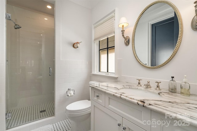 bathroom with toilet, vanity, tile walls, wainscoting, and a stall shower