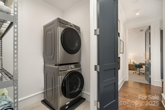 clothes washing area featuring stacked washer / dryer, laundry area, baseboards, and wood finished floors