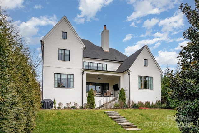 back of property featuring ceiling fan, a chimney, stairway, and a lawn