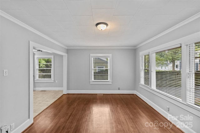 empty room with dark hardwood / wood-style flooring, ornamental molding, and a healthy amount of sunlight