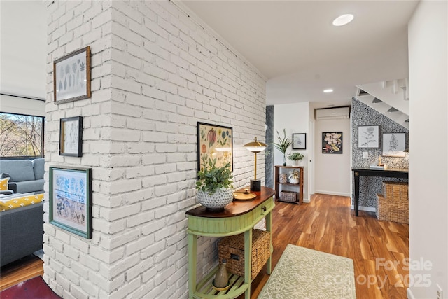 hallway featuring hardwood / wood-style flooring, a wall unit AC, and brick wall