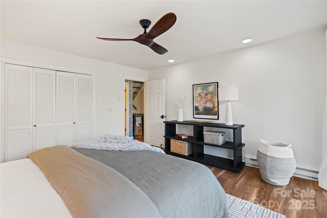 bedroom with hardwood / wood-style floors, a closet, ceiling fan, and a baseboard heating unit