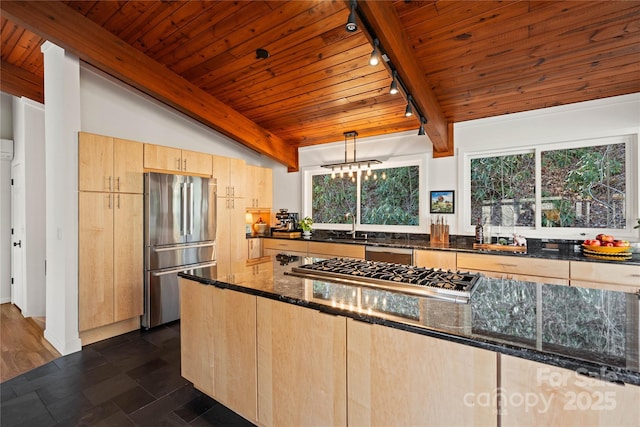 kitchen featuring appliances with stainless steel finishes, dark stone countertops, light brown cabinets, and decorative light fixtures