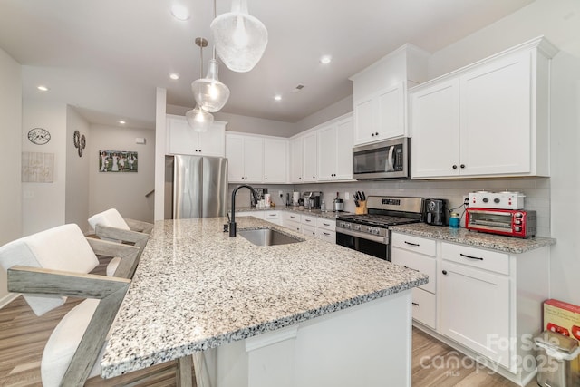 kitchen with stainless steel appliances, a kitchen island with sink, sink, and white cabinets