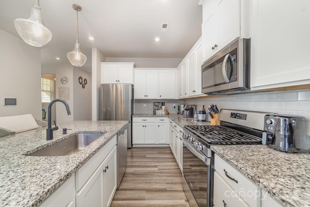 kitchen featuring sink, white cabinetry, stainless steel appliances, light stone counters, and decorative light fixtures