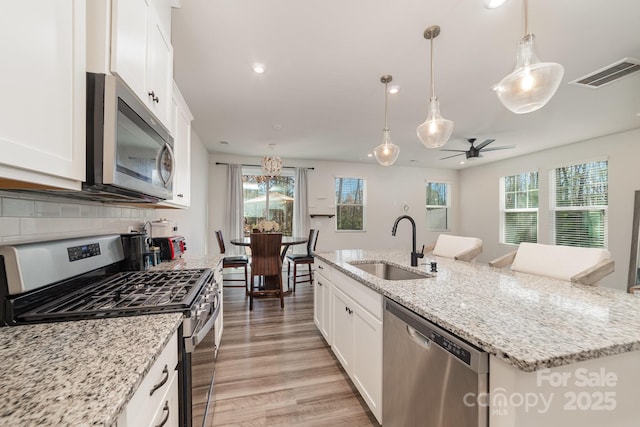 kitchen featuring sink, appliances with stainless steel finishes, pendant lighting, a kitchen island with sink, and white cabinets