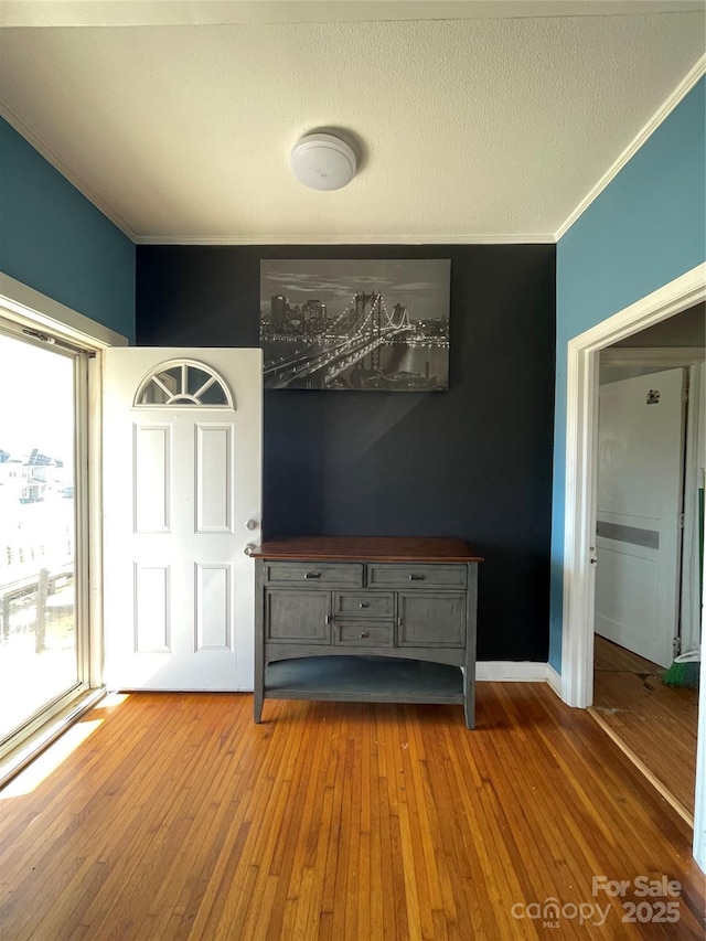 interior space with hardwood / wood-style flooring, a textured ceiling, baseboards, and crown molding