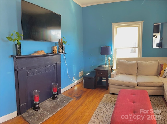 living room featuring a fireplace with flush hearth, baseboards, and wood finished floors