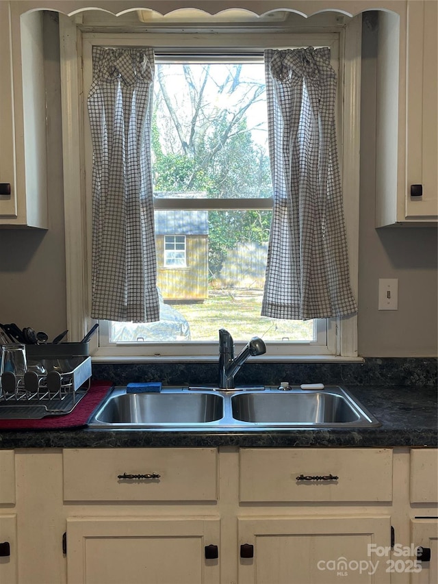 kitchen featuring dark countertops, white cabinets, and a sink