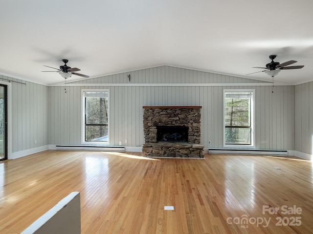 unfurnished living room with lofted ceiling, a baseboard heating unit, a stone fireplace, and wood finished floors