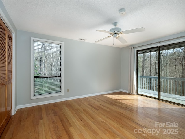 spare room featuring light wood-style floors, baseboards, visible vents, and a wealth of natural light