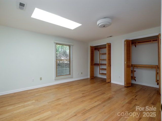 unfurnished bedroom with a skylight, visible vents, baseboards, light wood-style floors, and multiple closets