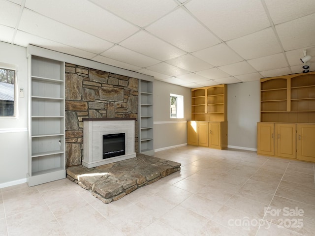 unfurnished living room featuring a fireplace, baseboards, and a drop ceiling