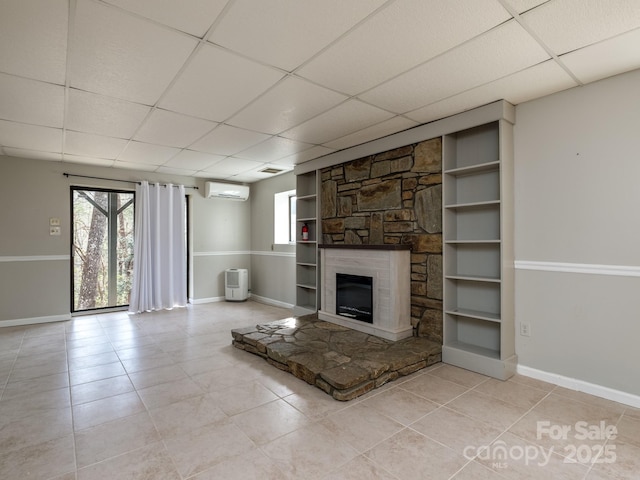 unfurnished living room featuring baseboards, built in features, an AC wall unit, a stone fireplace, and light tile patterned flooring