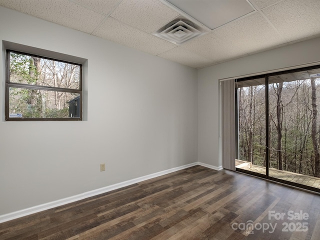 empty room with dark wood-style floors, a drop ceiling, and plenty of natural light