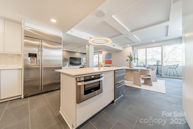 kitchen with stainless steel appliances, white cabinets, decorative light fixtures, a center island, and coffered ceiling