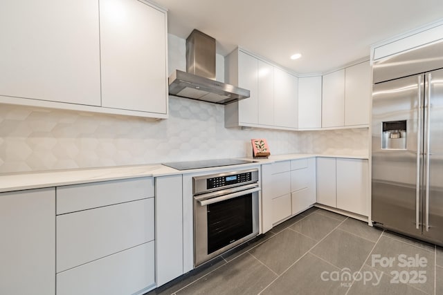 kitchen with white cabinetry, stainless steel appliances, tasteful backsplash, dark tile patterned flooring, and wall chimney exhaust hood