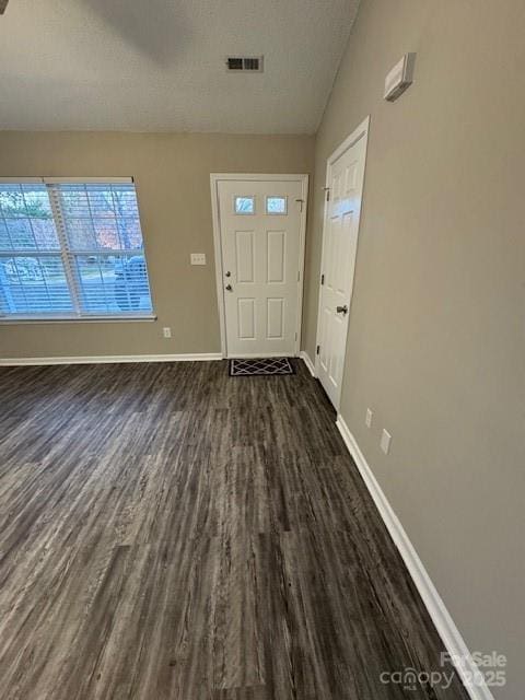 foyer entrance featuring a textured ceiling, dark wood-style flooring, visible vents, and baseboards