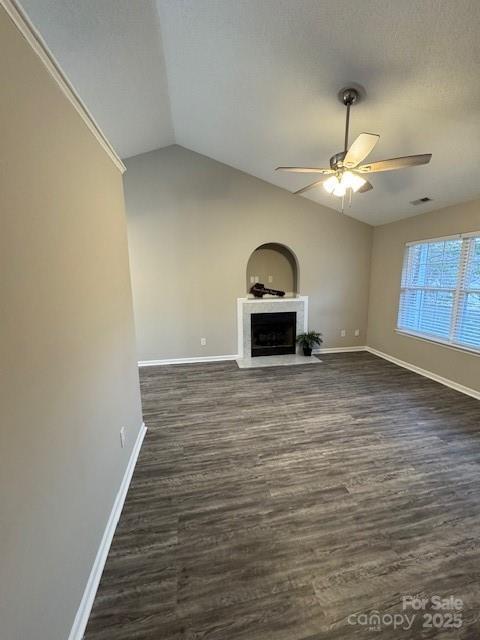 unfurnished living room featuring baseboards, dark wood-style floors, a fireplace with flush hearth, ceiling fan, and vaulted ceiling