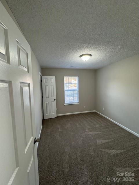 unfurnished room featuring baseboards, dark carpet, and a textured ceiling