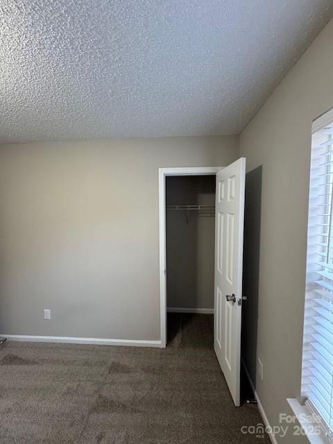 unfurnished bedroom featuring a textured ceiling, baseboards, a closet, and carpet flooring