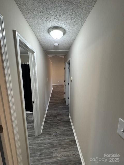 corridor with dark wood-style flooring, a textured ceiling, and baseboards