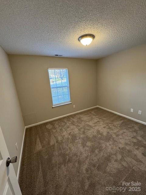 empty room featuring carpet floors, visible vents, a textured ceiling, and baseboards