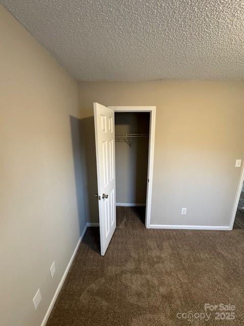 unfurnished bedroom featuring a closet, dark carpet, a textured ceiling, and baseboards