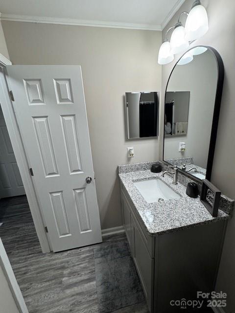 bathroom with a chandelier, wood finished floors, vanity, baseboards, and crown molding