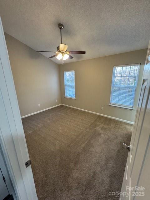 unfurnished room featuring a textured ceiling, dark colored carpet, a ceiling fan, and baseboards