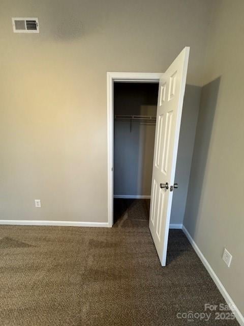 unfurnished bedroom featuring a closet, visible vents, dark carpet, and baseboards