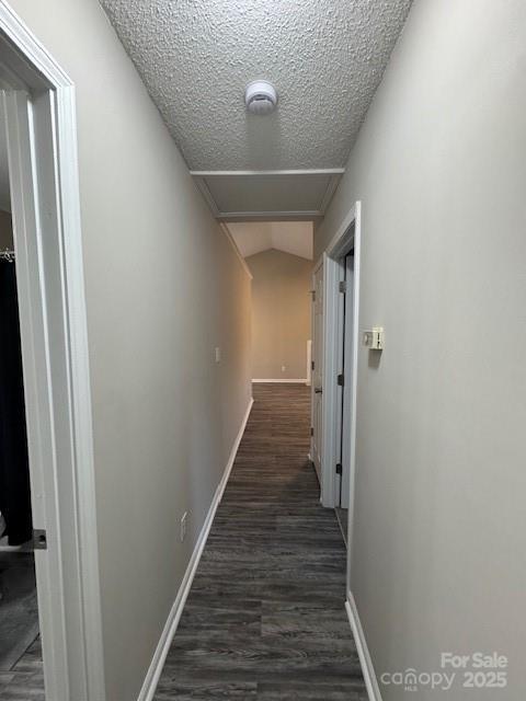 hall featuring baseboards, dark wood finished floors, and a textured ceiling