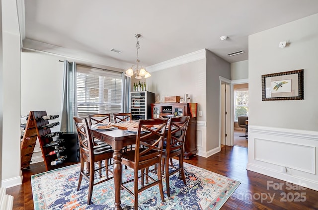 dining area featuring an inviting chandelier, visible vents, wood finished floors, and wainscoting