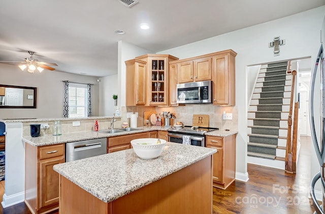 kitchen with stainless steel appliances, a peninsula, a sink, decorative backsplash, and light stone countertops