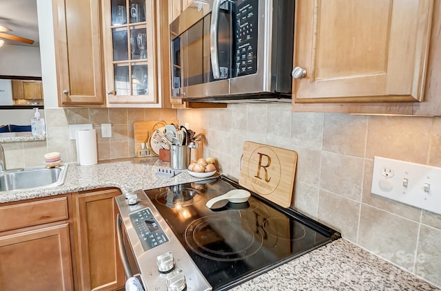 kitchen featuring tasteful backsplash, range with electric cooktop, glass insert cabinets, stainless steel microwave, and light stone counters