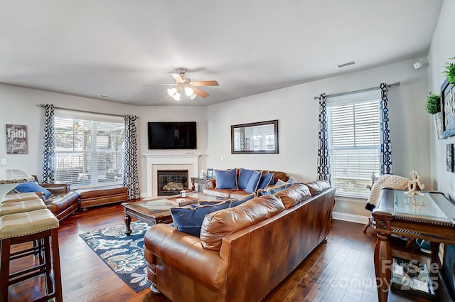 living room with dark wood-style flooring, a glass covered fireplace, a ceiling fan, and baseboards