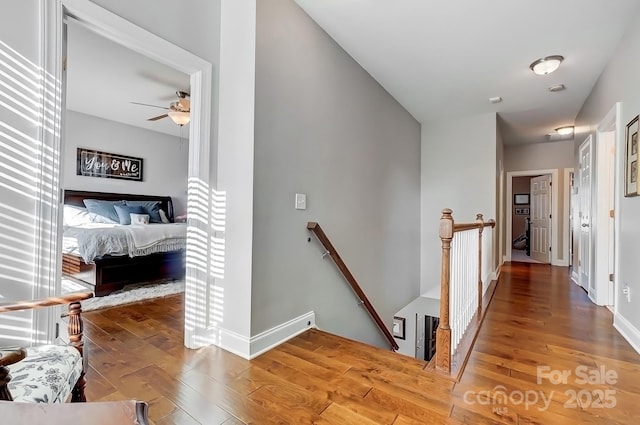 corridor featuring baseboards, wood finished floors, and an upstairs landing