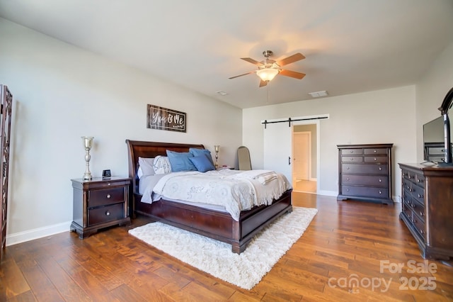 bedroom featuring dark wood-style floors, a barn door, visible vents, and baseboards