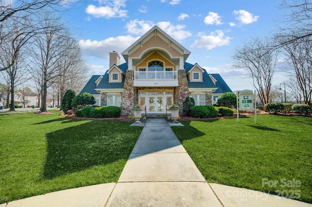 view of front of home featuring a balcony, stone siding, a front lawn, and french doors