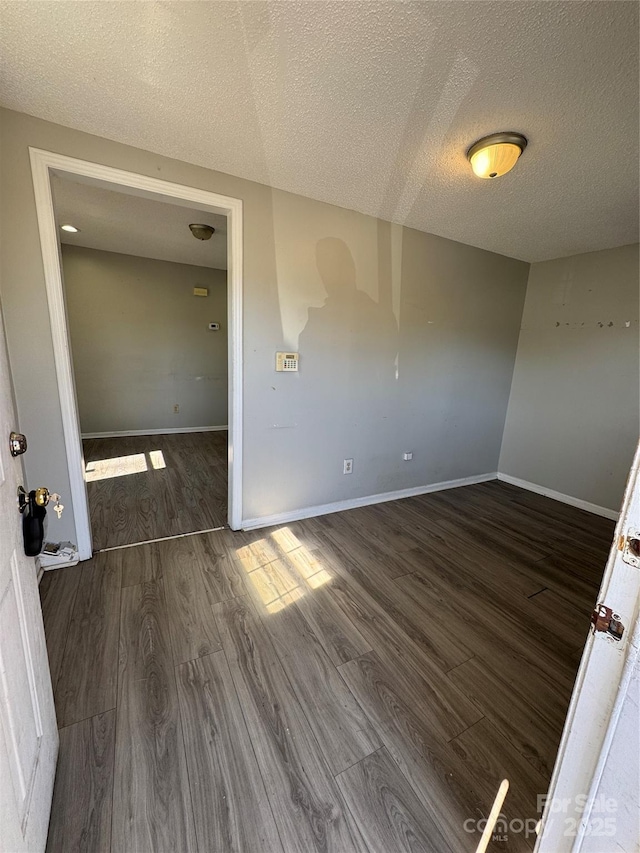 spare room with a textured ceiling, baseboards, and wood finished floors