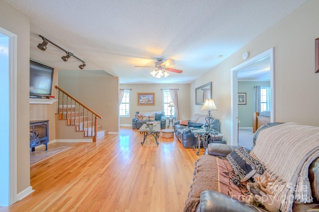 living room featuring ceiling fan, rail lighting, a textured ceiling, and light wood-type flooring