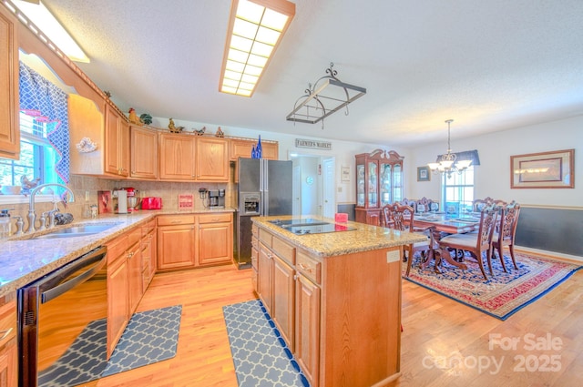 kitchen with sink, light hardwood / wood-style flooring, a kitchen island, pendant lighting, and black appliances