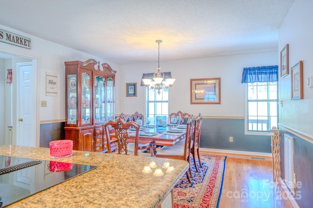 dining area with light hardwood / wood-style flooring, a wealth of natural light, a textured ceiling, and an inviting chandelier